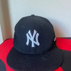 Svart New Era Yankees keps 7 1/4 - Klassisk svart New York Yankees keps från New Era Cooperstown Collection. Kepsen har en rak skärm, broderad NY-logga i vitt framtill och New Era-logga på sidan. Materialet är bomull och modellen är 59FIFTY fitted. Perfekt för dig som gillar streetwear och sport.