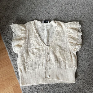 Vit spetsig stickad topp från Zara - Supersöt beige topp från Zara med volangärmar och v-ringning. Toppen har fina spetsdetaljer och knappar framtill. Är ganska kort men med ett linne under jättefin. Har alldrig kommit till andvändning så den är som ny .