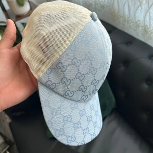 Gucci ljusblå keps med mesh - Snygg keps från Gucci i ljusblått med klassiskt GG-mönster över hela framsidan. Baksidan är i beige mesh för extra ventilation och cool vibe. Justerbar rem baktill för perfekt passform. Perfekt accessoar för att lyfta din streetstyle.