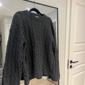 Mörkgrå kabelstickad tröja H&M - Mysig mörkgrå kabelstickad tröja från H&M i storlek S. Tröjan har rund halsringning, långärmade ärmar och en loose fit. Perfekt för kyliga dagar och enkel att styla med jeans eller kjol.