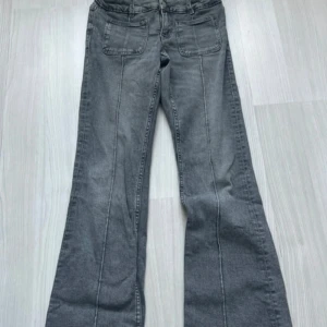 Grå bootcut jeans från Gina Tricot - Snygga grå jeans från Gina Tricot i bootcut-modell med raka ben som blir vidare nedtill. Jeansen har fram- och bakfickor, bälteshällor och dragkedja. Perfekta för dig som gillar en avslappnad men trendig look.