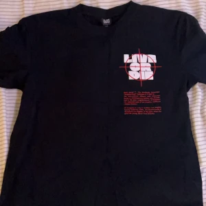 Svart Black Squad t-shirt XS - Svart oversized t-shirt från Black Squad i storlek XS. Stor vit text med röd måltavla och texten 'LIVE OR DIE' på både fram- och baksida. Skön passform och cool streetstil, perfekt för dig som gillar statement-plagg.