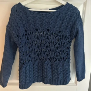 Unik Blå stickad tröja med flätmönster - Säljer en blå stickad tröja med snyggt flätmönster och hålstickade detaljer på bröstet och magen. Tröjan har rund halsringning och långa ärmar, perfekt för lager-på-lager och chill stil.