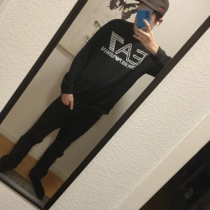 Svart långärmad tröja från EA7 - Svart långärmad tröja från EA7 Emporio Armani med stor vit logga framtill. Klassisk rund halsringning och relaxed fit. Perfekt för dig som gillar stilrena och sportiga plagg med tydlig branding.