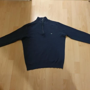 Blå half zip-tröja från Fynch-Hatton - Mörkblå långärmad tröja från Fynch-Hatton i mjuk bomull. Tröjan har en stilren half zip-dragkedja vid halsen och en liten broderad logga på bröstet. Perfekt för lager-på-lager och chill höstkvällar.