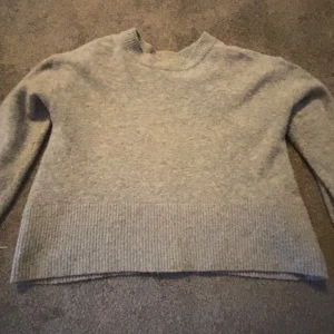 Grå stickad tröja från Gina Tricot - Mysig grå stickad tröja från Gina Tricot med ribbade detaljer vid hals, ärmslut och nederkant. Tröjan har en klassisk rund halsringning och lång ärm, perfekt för lager på lager under kyliga dagar.