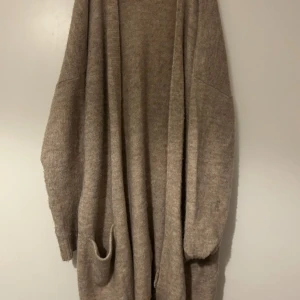 Beige stickad kofta från 157 - Mysig och oversized beige stickad kofta från 157. Koftan har långa ärmar, öppen front och stora fickor framtill. Perfekt för lager-på-lager och chill dagar. Enkel att matcha med allt i garderoben.