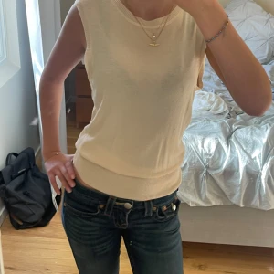 Beige stickad ärmlös topp - Säljer en  beige stickad topp med rund halsringning och ärmlös design. Toppen har en snygg ribbad kant vid hals och nederkant samt en liten knappdetalj och öppning i ryggen. Perfekt att matcha med jeans eller kjol! Storleken är m fast passar mig som har xs-s