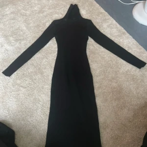 Svart ribbad långärmad poloklänning - Svart  långklänning från Giorgia med lång ärm och polokrage. Klänningen är ribbstickad och har en tight passform som framhäver siluetten. Perfekt för dig som gillar minimalistisk och stilren look.