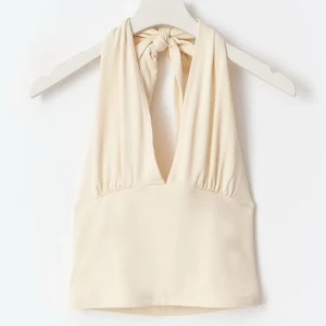 Beige halterneck topp Gina Tricot - Säljer en beige halterneck topp från Gina Tricot med djup v-ringning och knyt i nacken. Toppen är ärmlös och har en croppad passform, perfekt till sommaren. Tillverkad i mjukt och stretchigt material som sitter snyggt på kroppen.
