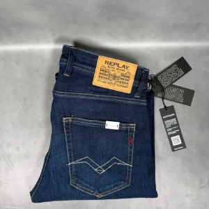 Replay Anbass jeans mörkblå herr - Snygga mörkblå Replay Anbass jeans med klassisk femficksdesign och kontrastsömmar. Jeansen har normal passform och raka ben, tillverkade i mjukt denimtyg med diskret tvätt. Märkespatch bak i midjan och detaljerade bakfickor.