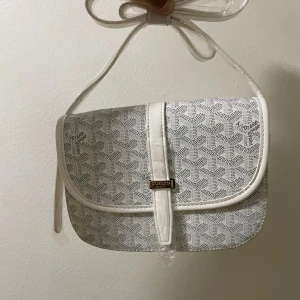 Vit axelväska  - Snygg vit axelväska med klassiskt mönster och silverfärgad logga framtill. Väskan har justerbar axelrem och stängs med ett stilrent spänne. Kommer med original dustbag, box och kort. Perfekt för dig som vill ha en exklusiv och trendig accessoar.