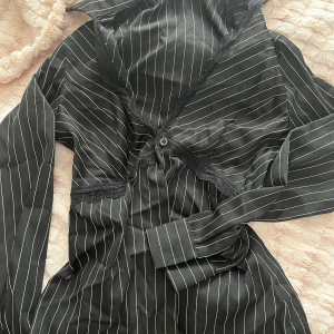 Svart randig skjorta med spets från SHEIN - Svart skjorta från SHEIN med tunna vita ränder och snygga spetsdetaljer längs v-ringningen. Skjortan har lång ärm, klassisk krage och knäppning framtill. 