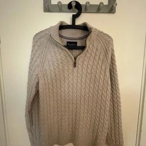 Bondelid kabelstickad half zip - Klassisk kabelstickad half zip i varm beige ton. Tidlös design utan logotyp för en ren och stilren look. Mjuk bomullsblandning som är bekväm både till vardags och lite mer uppklätt. använd men välvårdad. Mindre tecken på slitage såsom lätt noppning och något lösare stickning på ett par ställen, men inget som stör helhetsintrycket.