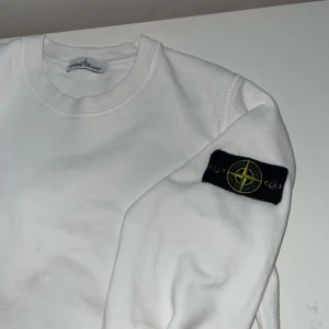 Stone Island tröja - Vit sweatshirt från Stone Island med klassisk rund hals och ribbade muddar. Tröjan har den ikoniska svarta logotypen med kompass på vänster ärm. . Svarar på alla frågor.