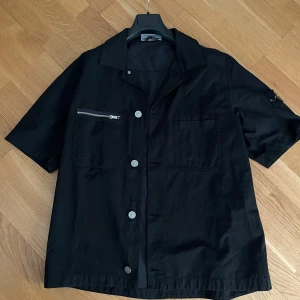 Svart kortärmad overshirt med dragkedja - Svart Stone Island overshirt med korta ärmar. Storlek M. Köparen står för frakt 📦 köpt på Stone Island butiken i Stockholm.