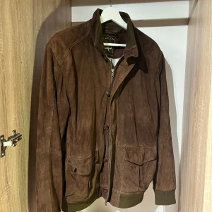 Brun mockajacka  - Brun mockajacka, liknande som valstarino jacka. Strl 50 i nacken men passar 48 (M/L) sparsamt använd men spår på användning finns. Pris satt ex frakt