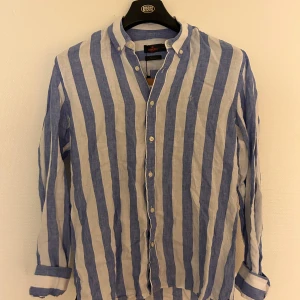 Blåvit randig linneskjorta Morris - Snygg blåvit randig skjorta från Morris i ren linne. Skjortan har klassisk krage, knappar framtill och långa ärmar. Perfekt för dig som gillar en chill och fräsch stil. Passar dig som vill ha något luftigt och stilrent.