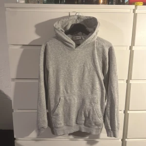 Grå hoodie från Weekday XS - Snygg ljusgrå hoodie från Weekday i storlek XS. Tröjan har en klassisk huva, magficka och ribbade muddar vid ärmslut och nederkant. Perfekt för chill dagar och enkel att matcha med jeans eller joggers. Mjuk insida i bomullsmix för extra komfort.