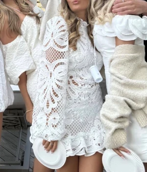 Vit spetsklänning med volang stundetklänning - Superfin vit kortklänning med spets och broderade detaljer. Klänningen har långärmade puffärmar, hög hals och volangkant nedtill. Genombrutet mönster och figurnära passform ger en r trendig vibe. Perfekt för student eller sommarens alla tillfällen. Tror det är ungefär samma klänning som på första bilderna skriv för fler, vet ej märket