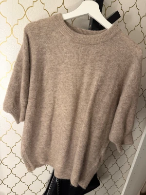 Beige stickad tröja Twist & Tango - Säljer en beige stickad tröja från Twist & Tango i storlek M. Tröjan har rund hals, korta ärmar och är gjord i ett mjukt material med ribbade detaljer vid hals och ärmslut. Perfekt för lager-på-lager och chill stil.