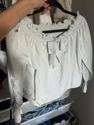 Ljusblå blus med rosett från Divided - Supersöt vit blus från Divided med smockad offshoulder-ringning och en fin rosettdetalj framtill. Endast använd 1 gång och sitter som en S💕💕