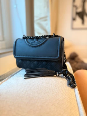 Svart quiltad axelväska Tory Burch - Säljer nu min matt svarta tory burch väska, denna väska tillverkas inte längre. Kvitto finns med och påsen, inköpt på NK i Göteborg 