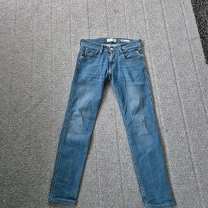Replay Anbass Slim Fit jeans blå - Snygga blå Replay Anbass Slim Fit jeans med klassisk femficksdesign och diskreta slitningar. Jeansen har smal passform, normal midja och är tillverkade i mjukt jeansmaterial med stretch. Perfekta för dig som gillar stilrena och moderna jeans.