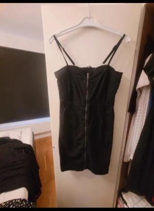 Svart kort klänning med snörning och dragkedja - Svart kort klänning med justerbara axelband, dragkedja framtill och cool snörningsdetalj på ryggen. Klänningen har en figurnära passform.