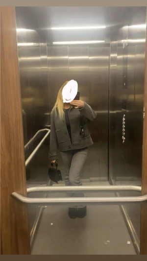 Grå kappa med knappar - Säljer en stilren grå kappa med klassisk rak passform och stora knappar framtill. Jackan har två fickor med lock och dekorativa detaljer vid ärmslutet. Perfekt för dig som gillar en clean och enkel look.