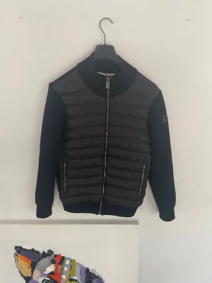 Moncler cardigan  - Snygg svart  från Moncler med quiltad front och släta ärmar. Jackan har två dragkedjeförsedda fickor, ribbad krage och Moncler-logga på ärmen. Perfekt för dig som vill ha en stilren och modern look.