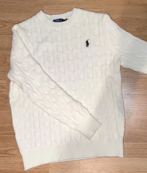 Vit stickad tröja Polo Ralph Lauren - Säljer en vit stickad tröja från Polo Ralph Lauren i storlek S. Tröjan har klassiskt kabelstickat mönster, rund hals och långärmad passform. På bröstet finns den ikoniska broderade loggan i svart. Perfekt för dig som gillar stilrena och tidlösa plagg.
