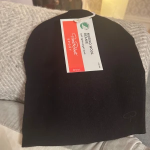 Svart merinoullmössa Pierre Robert - Svart mössa från Pierre Robert i mjuk och lätt merinoull med tencel. Enkel och stilren design, perfekt för kyliga dagar. Diskret Pierre Robert-logga broderad framtill. Svanenmärkt och tillverkad av 70% merinoull och 30% tencel.
