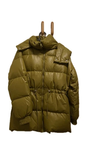 Olivgrön pufferjacka från kapphal - Säljer en oandvänd olivgrön pufferjacka med stor huva och snörning i midjan. Jackan har quiltad design, dragkedja framtill och elastiska muddar vid ärmslut. Ifrån kapphal