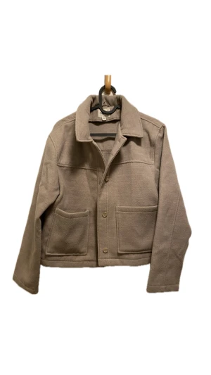 Beige jacka från KappAhl - Snygg beige overshirt från KappAhl med klassisk krage, stora framfickor och knäppning med knappar. Jackan har en rak och lite boxig passform, tillverkad i mjukt material som känns skönt mot huden. Perfekt att slänga på över en hoodie eller t-shirt.