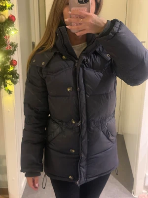 Boomerang jacka - Säljer en svart dunjacka med både dragkedja och knappar framtill. Jackan har hög krage, långa ärmar och praktiska fickor på sidorna. Perfekt för kalla dagar och har en snygg, puffig look som är riktigt trendig just nu.