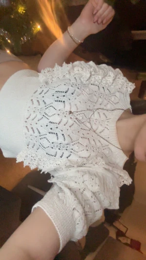 Vit croppad spetsblus med volang - Superfin vit croppad blus med spetsdetaljer och volang vid axlarna. Blusen har ett snyggt stickat mönster och är ärmlös med ribbad kant nedtill. Perfekt för dig som gillar romantisk och trendig stil.