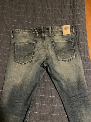 Replay Anbass jeans, blå, straight fit - Säljer ett par Replay Anbass jeans i klassisk blå tvätt med snygga slitningar och kontrastsömmar. Modellen har raka ben, fem fickor och normal passform. Märkesdetaljer syns på bakficka och insida midja. Perfekt för dig som gillar stilrena jeans med lite edge.