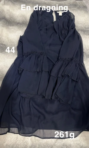 Mörkblå volangklänning stl 44 - Säljer en mörkblå klänning med volangdetaljer och långa ärmar. Klänningen har en luftig känsla och är tillverkad i ett tunt, lätt material som ger ett snyggt fall. Perfekt för dig som gillar en feminin och trendig look.🌸 Finns en dragning. Storlek 44