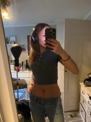 Grå croppad stickad polotopp Gina Tricot - Säljer en grå croppad stickad polotopp från Gina Tricot. Toppen har korta ärmar, ribbad kabelstickning och tre knappar framtill vid kragen. Perfekt för dig som gillar en chill och trendig look med lite preppy vibe.