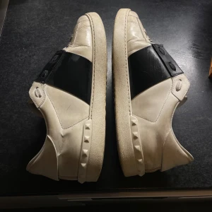 Valentino Garavani Open sneakers vit/svart - Säljer ett par Valentino Garavani Open sneakers i vitt skinn med bred svart läderdetalj över vristen. Storlek 42 men passar även 43. 