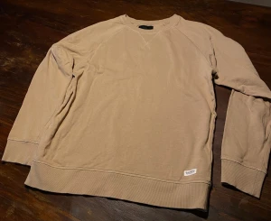 Beige sweatshirt från 157, storlek M - Säljer en stilren beige sweatshirt från 157 i storlek M. Tröjan har rund hals, ribbade muddar vid ärmslut och nederkant samt diskret logga vid höften. Perfekt för chill dagar och enkel att matcha med jeans eller joggers.