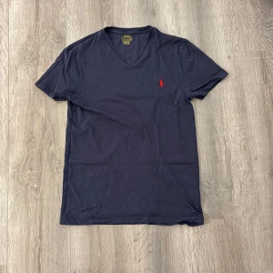  t-shirt Polo Ralph Lauren - Snygg mörkblå t-shirt från Polo Ralph Lauren med röd broderad logga på bröstet. Modellen är slim fit och har korta ärmar. Tillverkad i mjuk bomull som känns skön mot huden. Perfekt för dig som gillar klassisk stil med en modern touch.                  •Mycket bra skick 