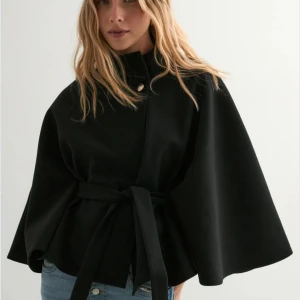 Nelly poncho kappa  - Snygg svart kappa från Nelly. Säljs inte längre. Den är aldrig använd och lappen sitter kvar. 