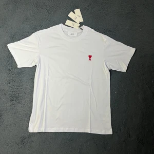 Ami paris T-shirt  - Helt ny ! Vit t-shirt från Ami Alexandre Mattiussi med klassisk passform och rund hals. På bröstet finns ett litet rött hjärta med A-bokstav. Tillverkad i mjuk bomull och har korta ärmar. Perfekt för en clean och stilren look.