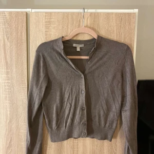 Brun kofta från H&M i bomull XS - En enkel brun kofta från H&M i storlek XS. Koftan har långa ärmar, rund halsringning och knäppning framtill med flera knappar. Tillverkad i mjuk bomull och passar perfekt till lager-på-lager-stil.