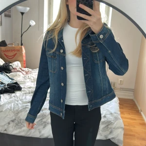 Mörkblå jeansjacka från Lee - Snygg mörkblå jeansjacka från Lee med klassisk krage och silverfärgade knappar framtill. Jackan har två bröstfickor med knapp. Står att det är storlek L men passar de som har XS/S då den är liten i storleken. 