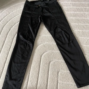 Svarta byxor med quiltade detaljer H&M - Svarta byxor från H&M med snygga quiltade partier längs sidorna och dragkedja framtill. Byxorna har smal passform och är tillverkade i en bomullsblandning med lite stretch. Perfekta för dig som gillar en stilren look med extra edge.