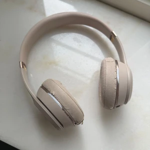 Beats Solo3 Wireless - Beats Solo3 Wireless over-ear hörlurar i beige med roséguld-detaljer. Hörlurarna fungerar men öronkuddarna har tydligt slitage och sprucken yta. Trådlös anslutning och ikonisk Beats-design. Perfekt för dig som vill ha bra ljud till ett lägre pris. (Går köpa nya kuddar till billigt). 