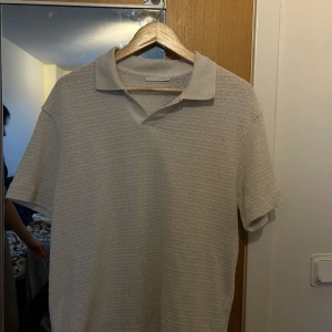 Beige piké t-shirt från Zara - Säljer en beige piké t-shirt från Zara i storlek M. T-shirten har korta ärmar, klassisk krage och ett diskret strukturerat tyg. Perfekt för en clean och stilren look.